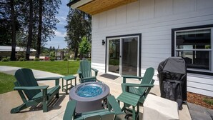 A patio with green Adirondack chairs, a round fire pit, and a grill.