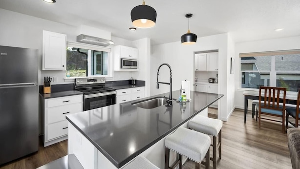 A modern kitchen with a central island, stainless steel appliances, white cabinetry, and pendant lighting.