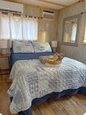Quarto com cama, duas mesas de cabeceira, espelho e janela com cortinas.