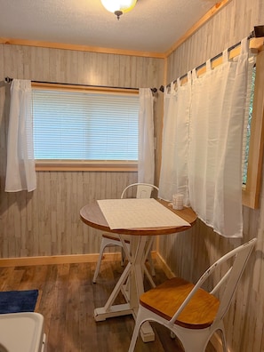 A room with a wooden paneled wall, a window with blinds, a table with chairs, and a ceiling fan.