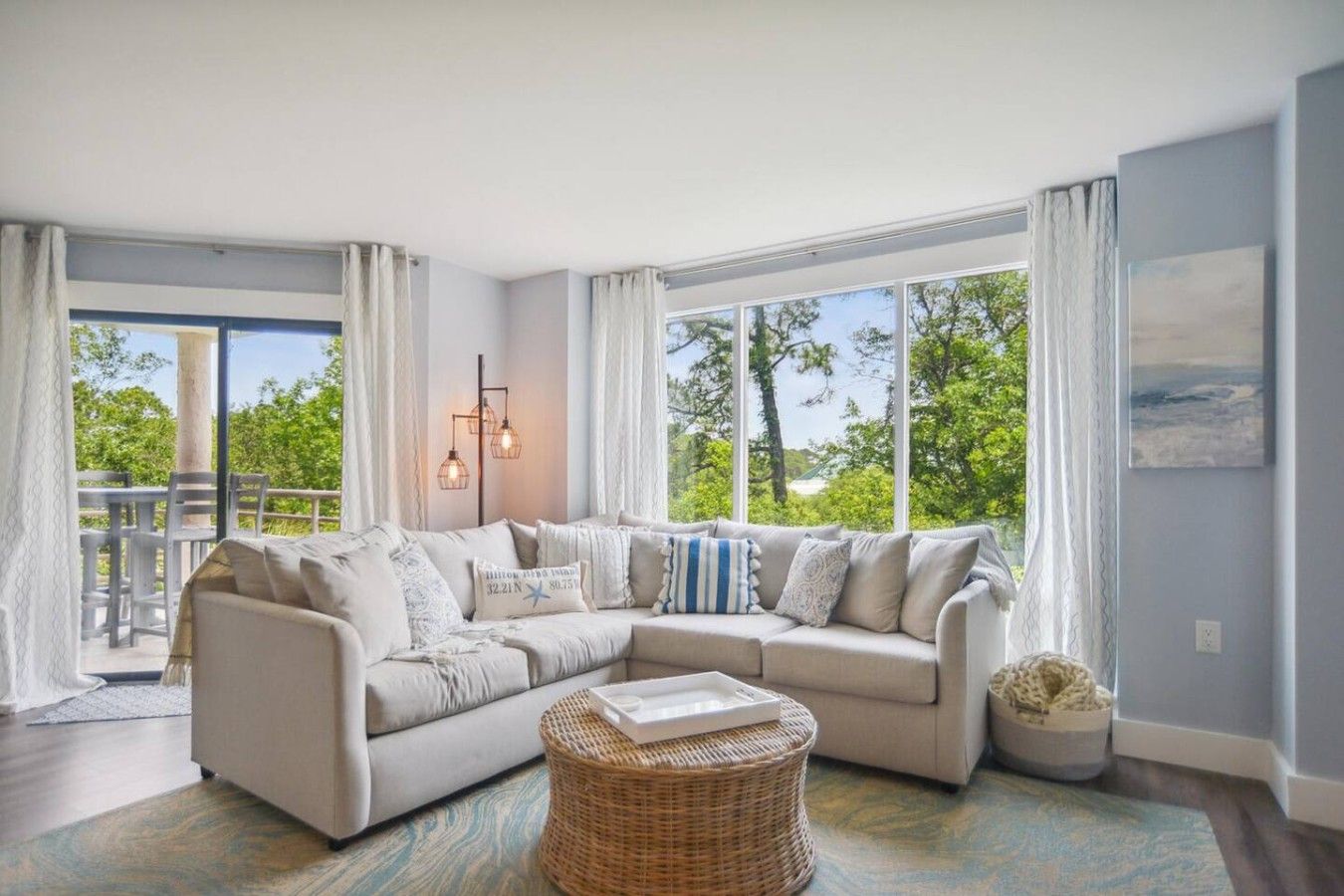 A modern living room with a sectional sofa, a wicker ottoman, and a dining area with a table and chairs.
