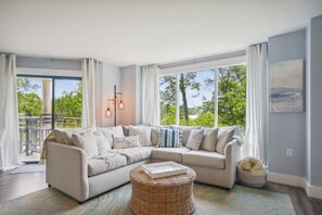 A modern living room with a sectional sofa, a wicker ottoman, and a dining area with a table and chairs.
