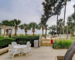 An outdoor patio area with a table and chairs, surrounded by greenery and palm trees.