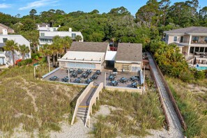 A beachfront property with a covered patio area, a swimming pool, and a beach access walkway.