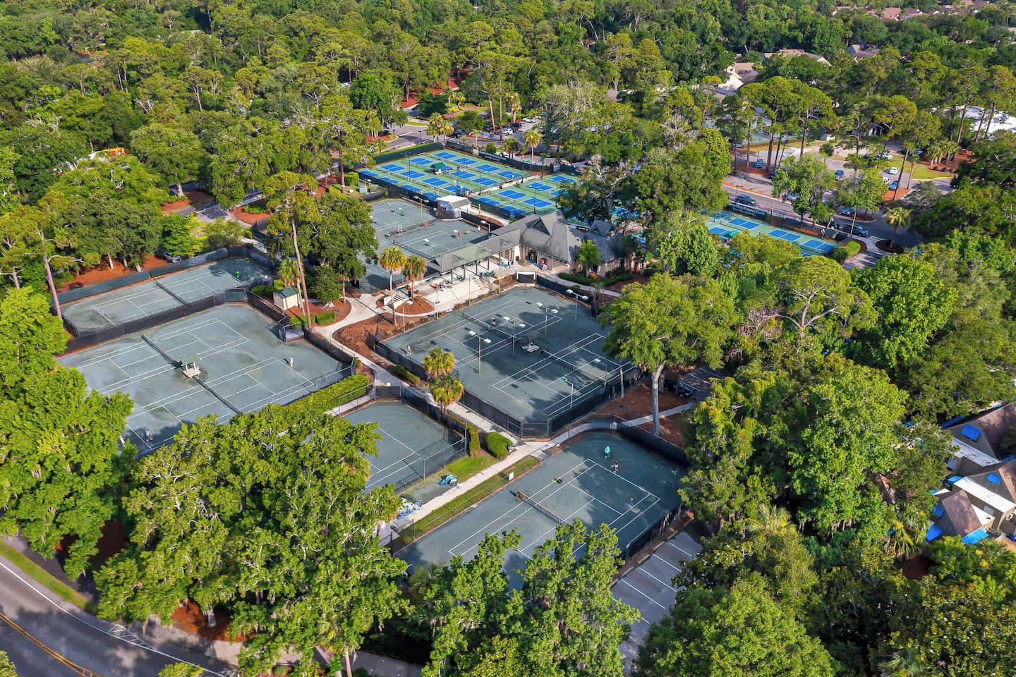 An aerial view of a residential area with multiple tennis courts surrounded by dense greenery.
