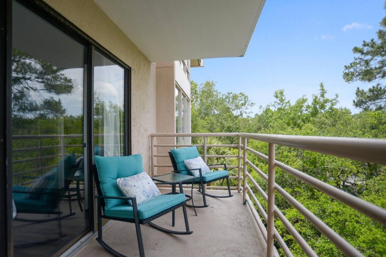 A balcony with two rocking chairs and a table, overlooking a lush green landscape.