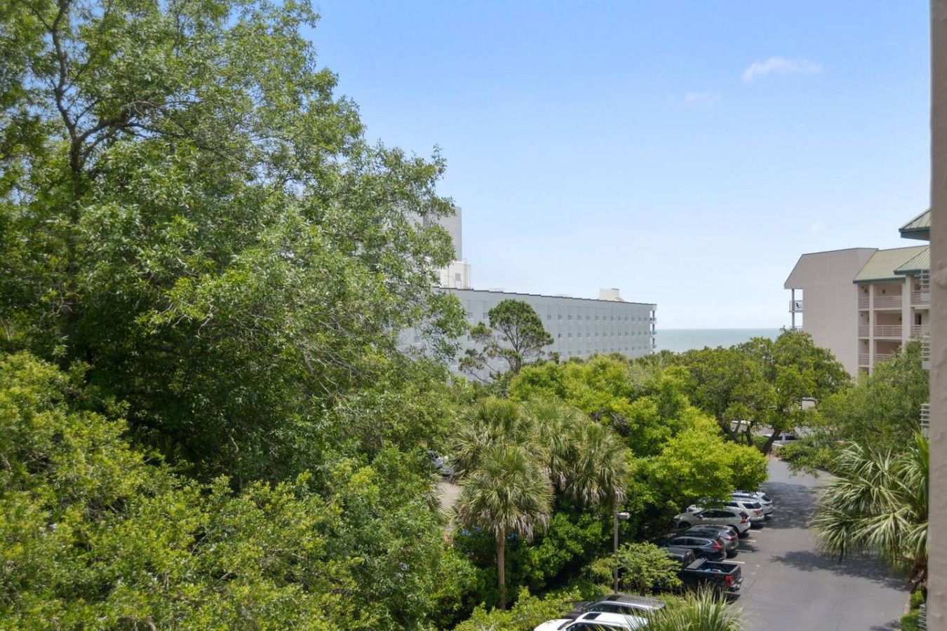 A hotel with a parking lot, surrounded by dense greenery and a clear view of the ocean.