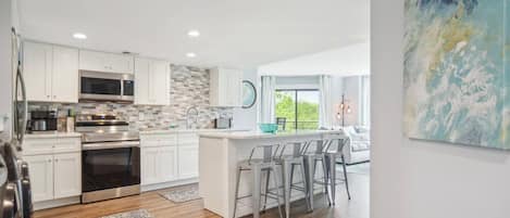 A modern kitchen with white cabinets, stainless steel appliances, and a herringbone tile backsplash.