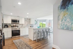 A modern kitchen with white cabinets, stainless steel appliances, and a herringbone tile backsplash.