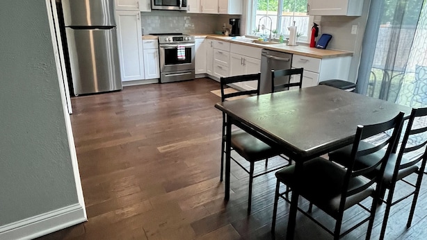 A modern kitchen with white cabinets, stainless steel appliances, and a wooden dining table with chairs. - 3BR/1BA BROKEN ARROW HOME (Broken Arrow)