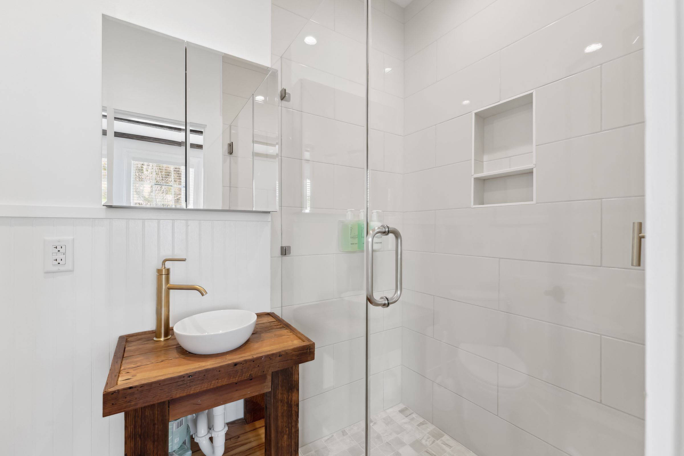 A modern bathroom with a wooden vanity, a white sink, and a glass-enclosed shower area.