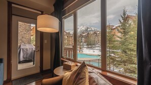A cozy room with a large window overlooking a snowy mountain and a pool. - Grotto Mountain Guesthouse (Canmore)