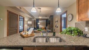 A modern kitchen with granite countertops, stainless steel sink, and pendant lighting. - Grotto Mountain Guesthouse (Canmore)