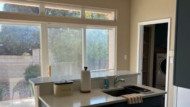 Eine moderne Küche mit großem Fenster, einem eingebauten Geschirrspüler und einer Arbeitsplatte mit Kaffeemaschine.