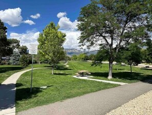 Stroll through the serene park, surrounded by trees and a winding path, with picnic tables and a scenic view of the mountains.