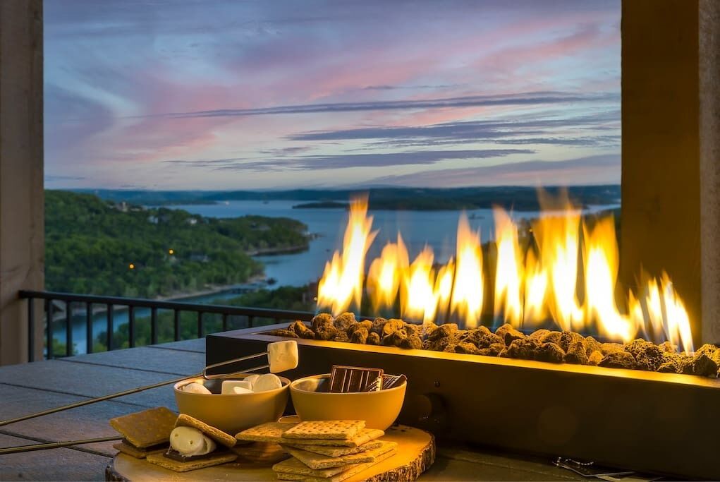 A fire pit with snacks and a view of a lake at dusk.