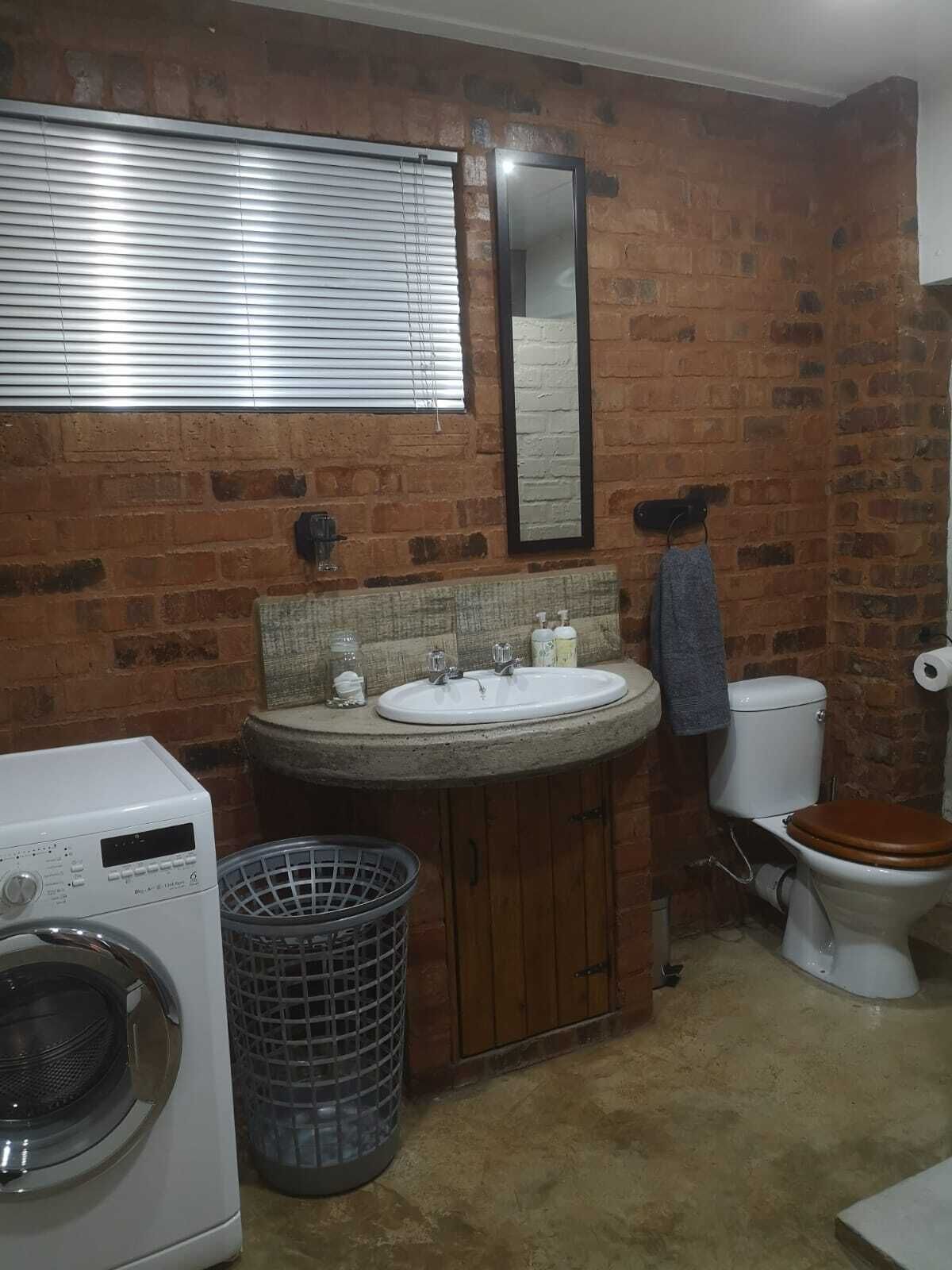 Baño pequeño con pared de ladrillo, un lavabo, inodoro, lavadora y cesto de ropa.