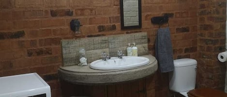 Baño pequeño con pared de ladrillo, un lavabo, inodoro, lavadora y cesto de ropa.