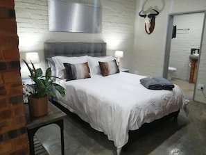 Ein Schlafzimmer mit einem Bett, Nachttischlampen, einer Topfpflanze und einem an der Wand befestigten Tierkopf.
