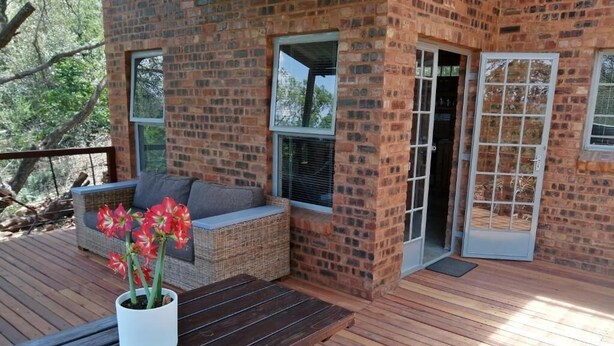 A wooden deck with a brick wall, a wicker sofa, and a table with a potted plant.
