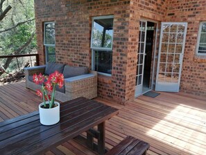 A wooden deck with a brick wall, a wicker sofa, and a table with a potted plant. - Boshoffville Family Farm (Pretoria)