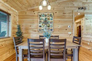 A wooden interior with a dining table surrounded by chairs, a Christmas tree, and a wall-mounted poster. - Gorgeous Gatlinburg Cabin: Large Deck & Hot Tub! (Gatlinburg)