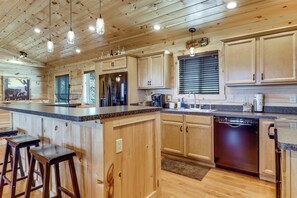 A kitchen with wooden cabinets, a stainless steel refrigerator, a dishwasher, and a bar area with stools. - Gorgeous Gatlinburg Cabin: Large Deck & Hot Tub! (Gatlinburg)