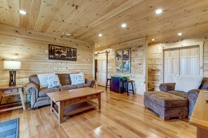 Ein Interieur einer Holzhütte mit einer Couch, einem Couchtisch und einem Esstisch.