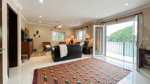 A spacious room with a large window, a black leather sofa, a patterned rug, and a view of a green hillside.