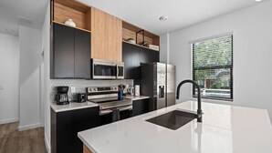 A modern kitchen with black cabinets, stainless steel appliances, a large island with a sink, and a window with blinds. - Gated Community  - Near Disney (Kissimmee)