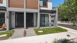 A modern two-story house with a front porch, a covered patio with chairs, and a well-maintained lawn. - Gated Community  - Near Disney (Kissimmee)