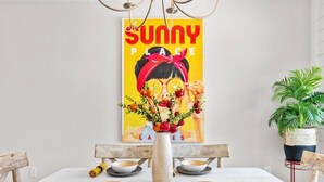 Ein Esstisch mit weißer Tischdecke, eine Vase mit Blumen und ein Poster an der Wand.