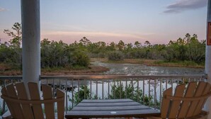 Eine Holzterrasse mit zwei Adirondack-Stühlen, die auf einen Fluss und Bäume blicken.