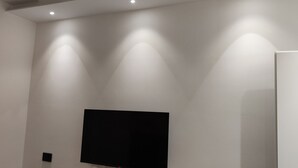 Una habitación con un televisor de pantalla plana grande montado en la pared, luces empotradas y una puerta blanca.