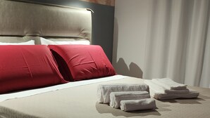 Una cama bien hecha con almohadas rojas y blancas, un cabecero y toallas dobladas sobre la cama.