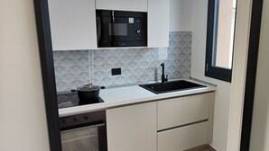 Una cocina compacta con microondas, estufa, lavaplatos y muebles blancos.