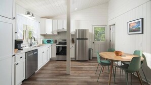 Eine moderne Küche mit weißen Schränken, Edelstahlgeräten und einem Essbereich mit einem Holztisch und grünen Stühlen.