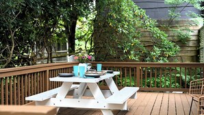 Eine Holzterrasse mit einem Picknicktisch für vier Personen, umgeben von einer Holzbrüstung und üppiger Vegetation.