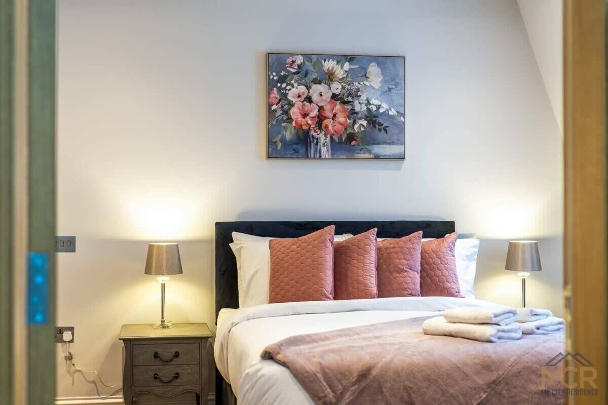 A hotel room with a bed, bedside lamps, a painting, and a nightstand.