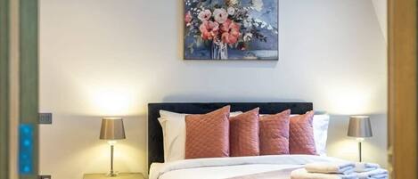A hotel room with a bed, bedside lamps, a painting, and a nightstand.