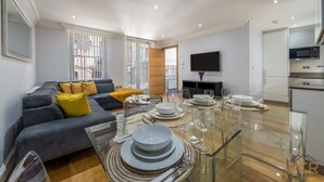 Un salon moderne comprenant un canapé, une table à manger pour quatre personnes et un coin cuisine équipé d’appareils électroménagers.