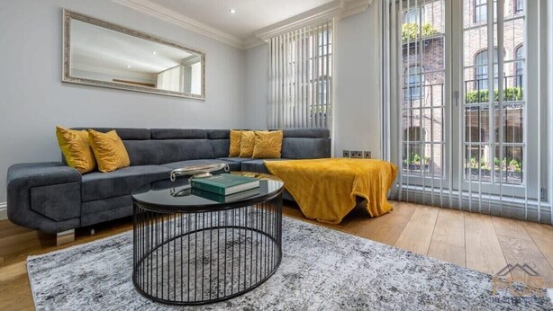 Un salon moderne avec un canapé gris, une table basse ronde et une grande fenêtre équipée de stores verticaux.