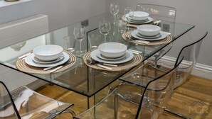Un espace de salle à manger moderne avec une table en verre, des chaises transparentes et de la vaisselle blanche.