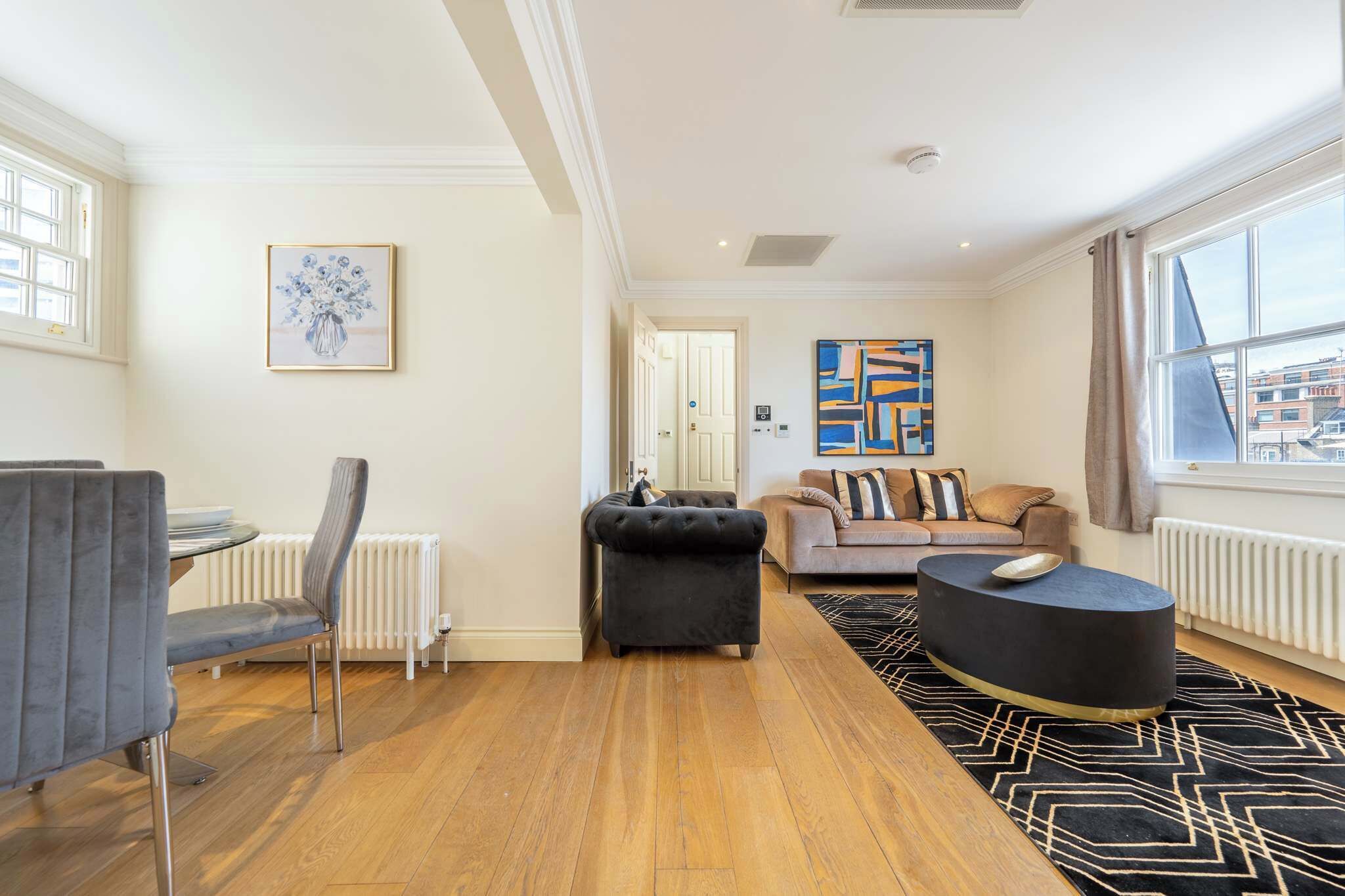 A modern living room with a dining area, a black ottoman, and a black coffee table.