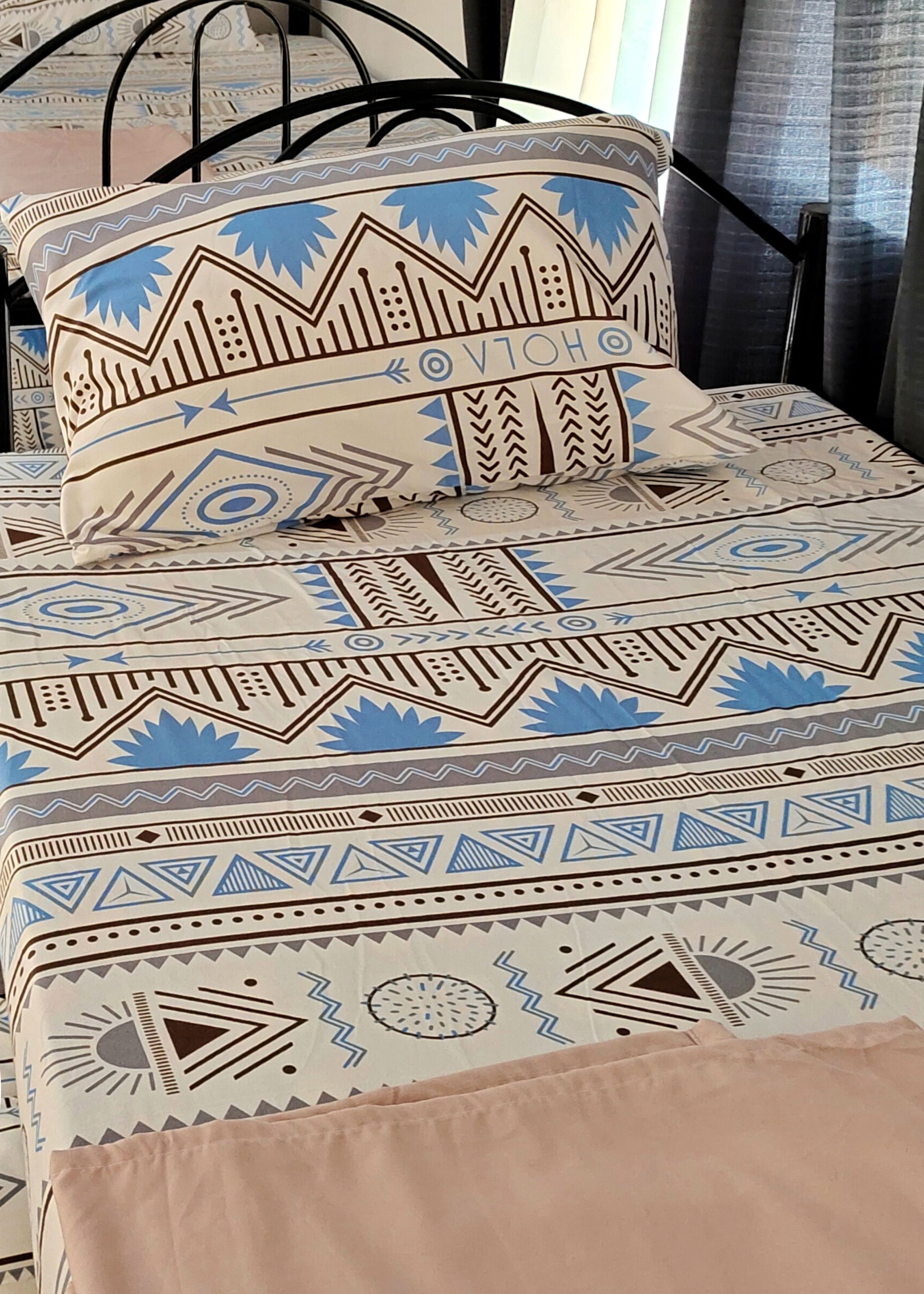 A bed with a patterned bedspread and pillows, a black metal frame, and a logo for Malungaya Apartments.