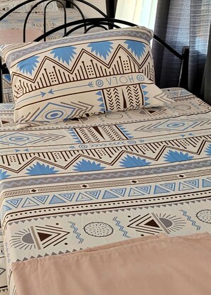 A bed with a patterned bedspread and pillows, a black metal frame, and a logo for Malungaya Apartments. - Malunggay Apartments (Mariveles)