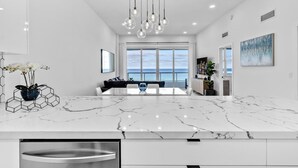 Una cucina moderna con un piano di lavoro in marmo, illuminazione a sospensione e vista sull'oceano.