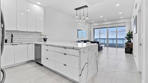 Una cucina moderna con mobili bianchi, un'isola in marmo e un'ampia finestra che si affaccia sul cielo.