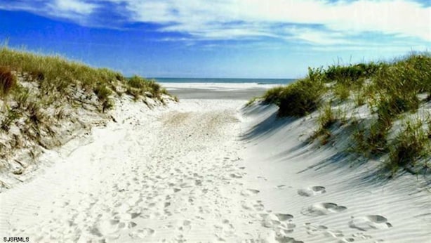 Ein sandiger Küstenpfad mit Fußabdrücken, der zum Meer führt, umgeben von Dünen.