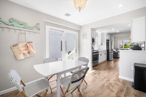 A modern kitchen with white cabinets, a black refrigerator, and a dining area with a white table and patterned chairs. - Beach Bungalow -- 1.5 Blocks to Beach! (Brigantine)